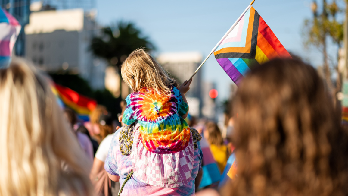 Parent and child carry Progress Pride flag